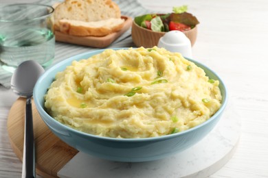 Photo of Bowl of tasty mashed potatoes with onion served on white wooden table