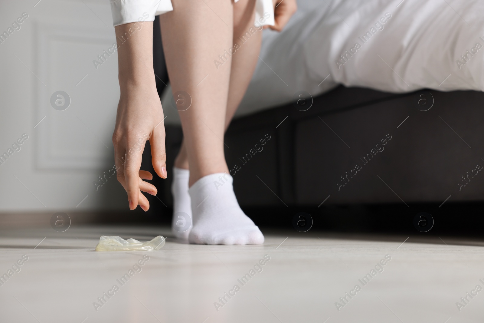 Photo of Woman taking unrolled condom from floor indoors, closeup. Safe sex