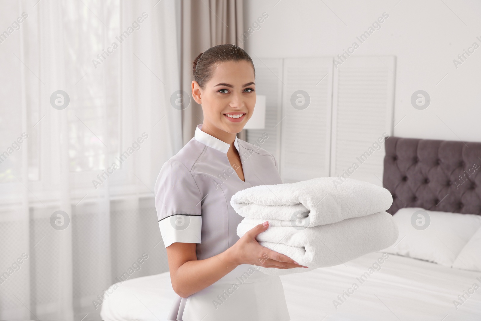 Photo of Young chambermaid with clean towels in bedroom