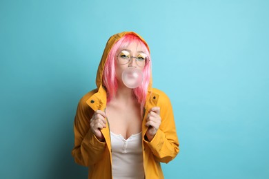 Fashionable young woman in pink wig with bright makeup blowing bubblegum on yellow background