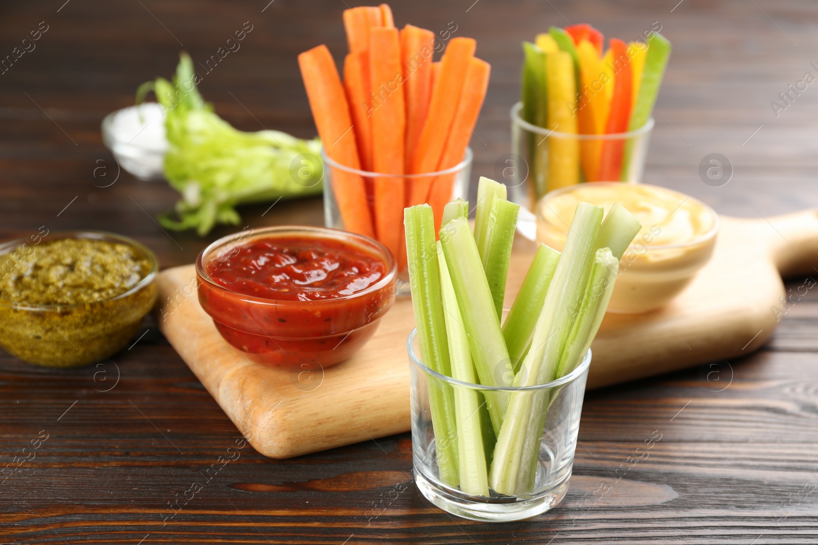 Photo of Celery sticks in glass bowl and dip sauce on wooden table