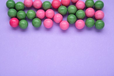 Many bright chewy gumballs on lilac background, flat lay. Space for text