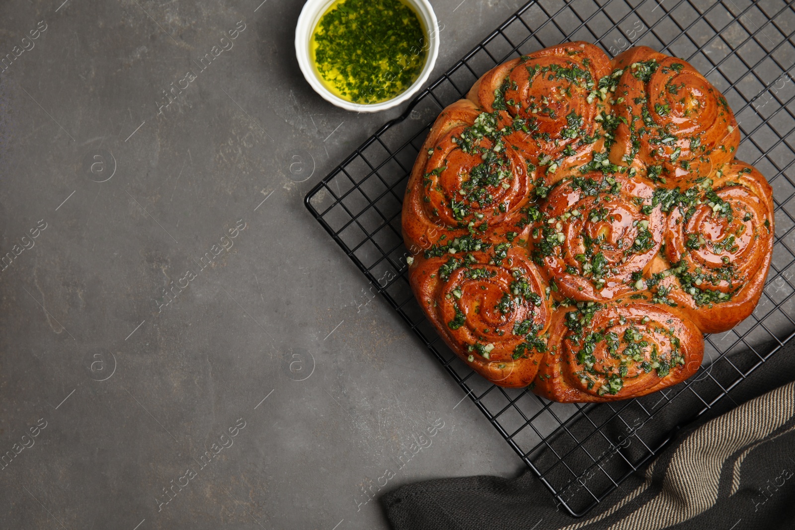 Photo of Traditional Ukrainian garlic bread with herbs (Pampushky) and aromatic oil on grey table, flat lay. Space for text