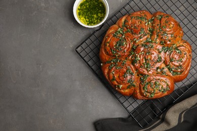 Photo of Traditional Ukrainian garlic bread with herbs (Pampushky) and aromatic oil on grey table, flat lay. Space for text