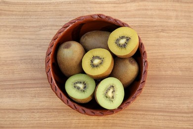 Photo of Bowl with many whole and cut fresh kiwis on wooden table, top view