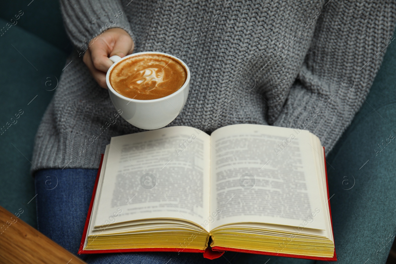 Photo of Woman with cup of coffee reading book at home, closeup