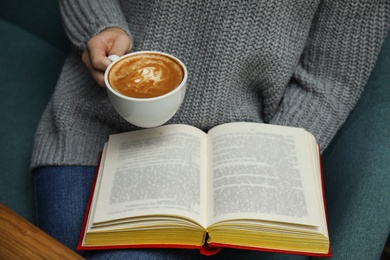 Woman with cup of coffee reading book at home, closeup