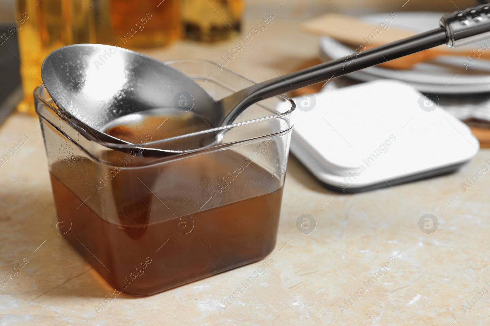 Photo of Container and ladle with used cooking oil on beige table