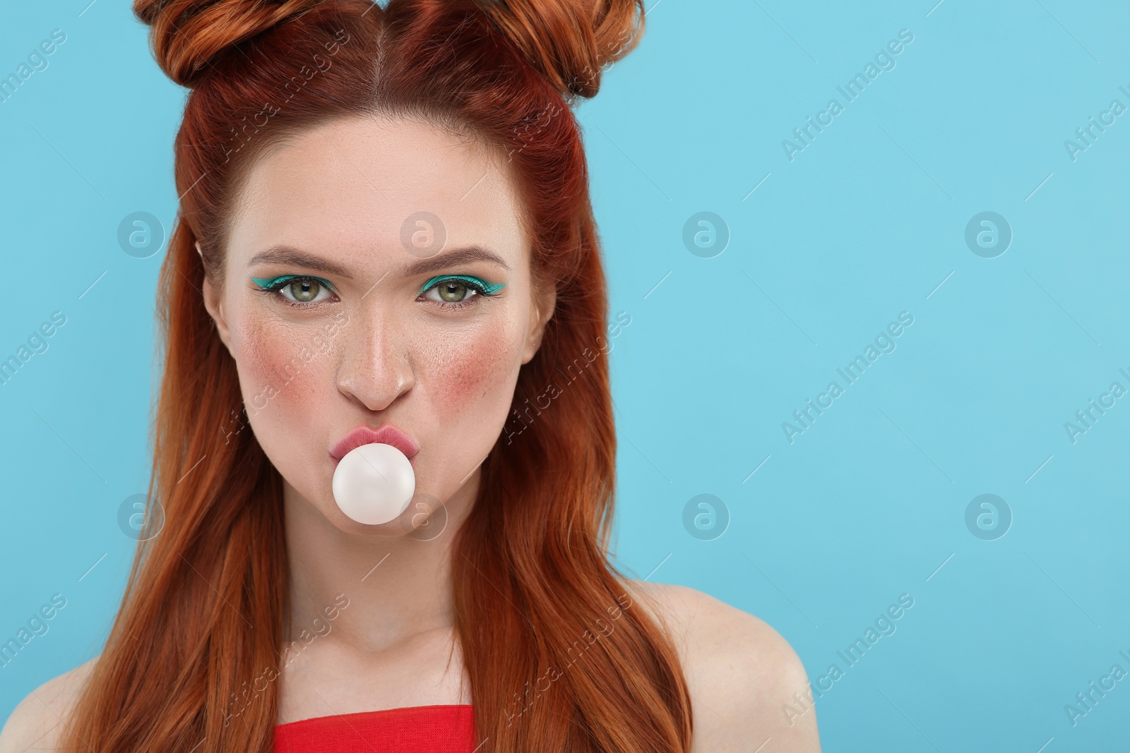 Photo of Portrait of beautiful woman with bright makeup blowing bubble gum on light blue background. Space for text