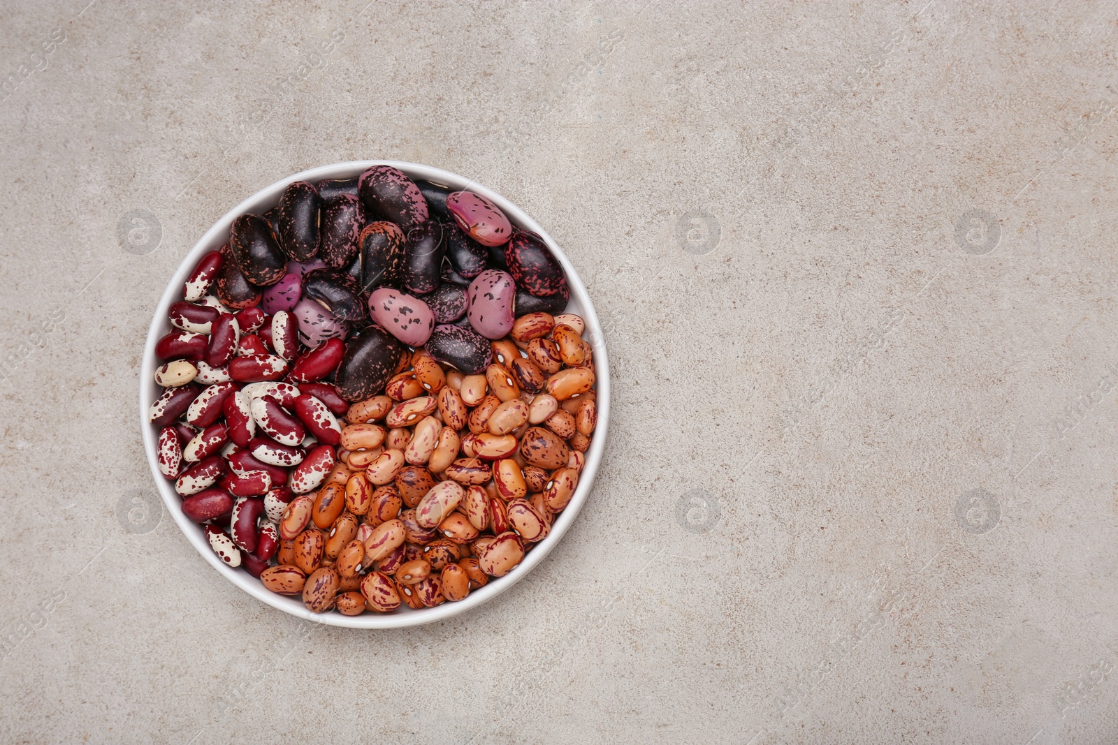 Photo of Bowl with different types of beans on light grey table, top view. Space for text