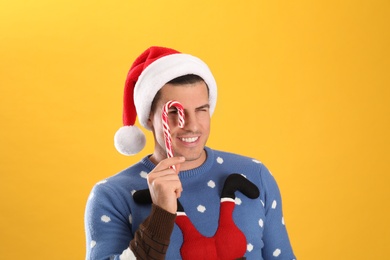 Handsome man in Santa hat holding candy cane on yellow background