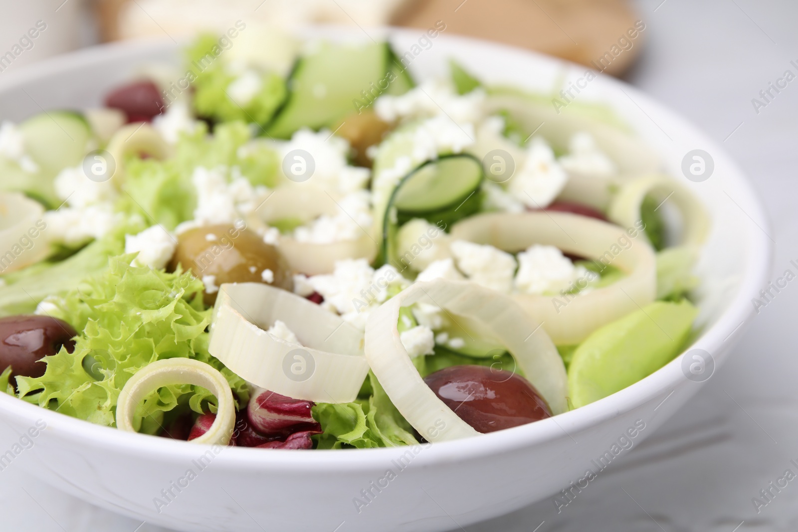 Photo of Bowl of tasty salad with leek, olives and cheese on white table, closeup