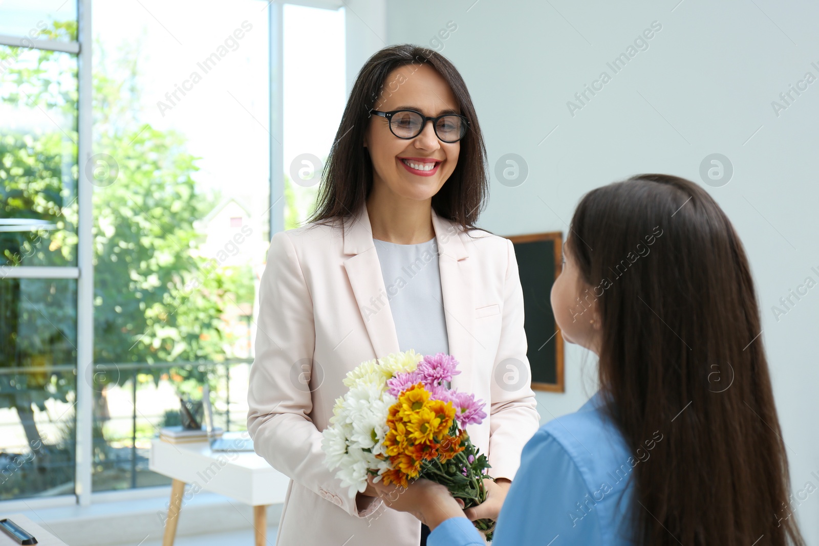 Photo of Schoolgirl congratulating her pedagogue with bouquet in classroom. Teacher's day