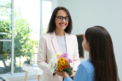 Photo of Schoolgirl congratulating her pedagogue with bouquet in classroom. Teacher's day