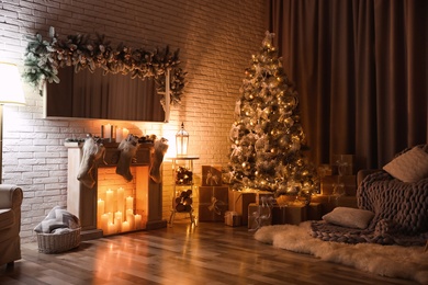 Stylish interior with beautiful Christmas tree and artificial fireplace at night