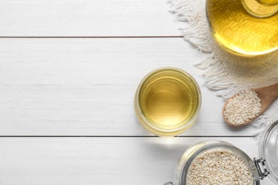 Jar of organic sesame oil and seeds on white wooden table, flat lay. Space for text