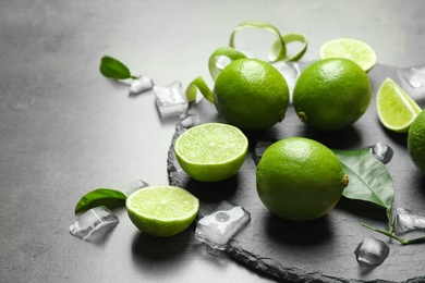 Photo of Slate plate with fresh ripe limes and ice cubes on gray background