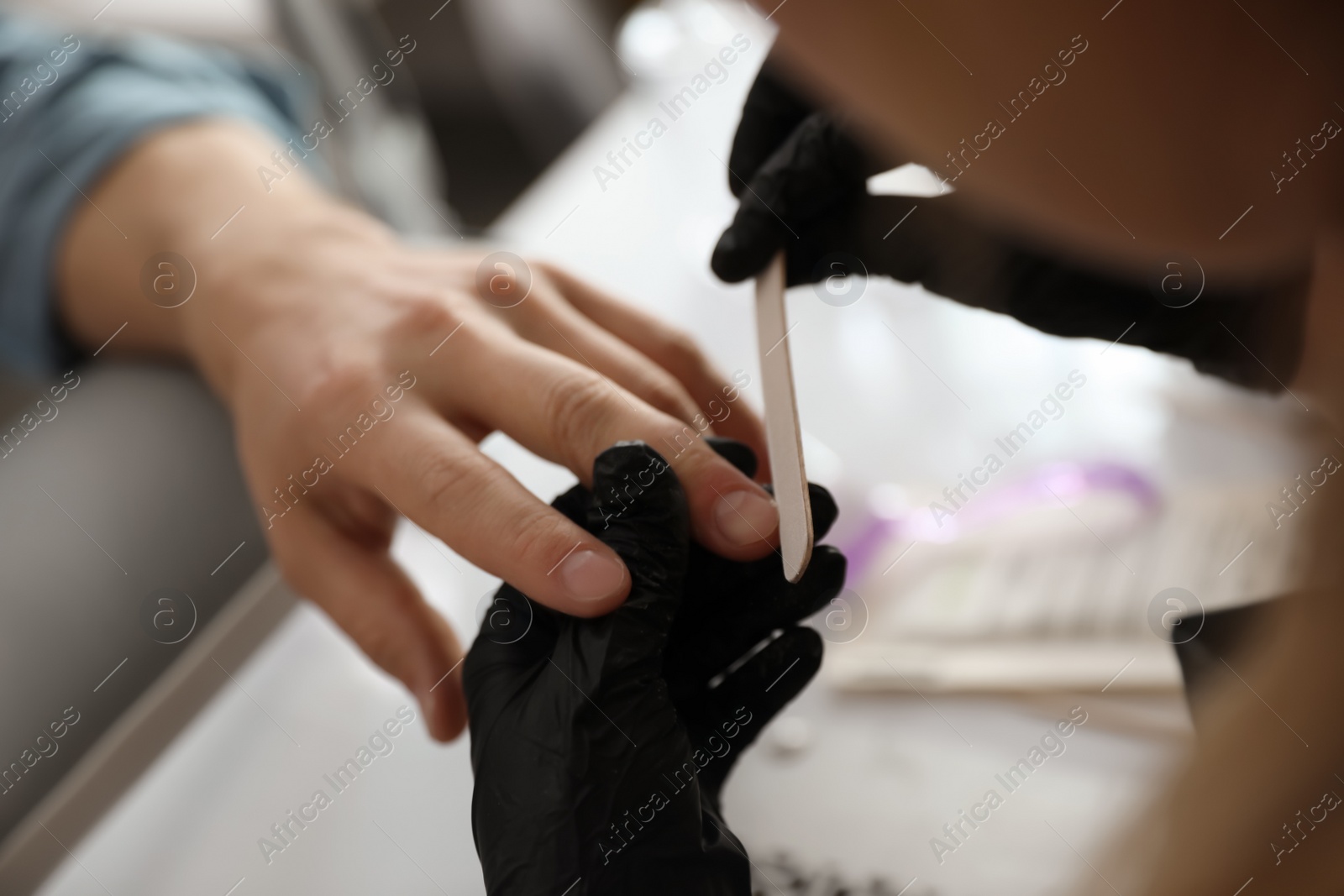 Photo of Professional manicurist filing client's nails in beauty salon, closeup