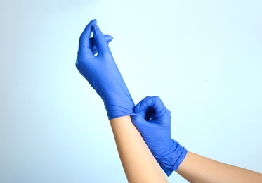 Woman putting on latex gloves against light blue background, closeup of hands