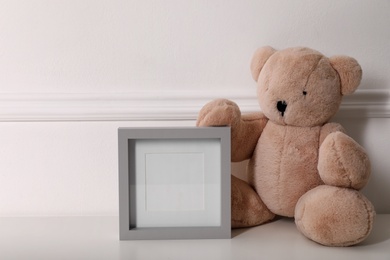 Photo of Empty photo frame and cute toy bear near wall, space for text. Baby room interior element