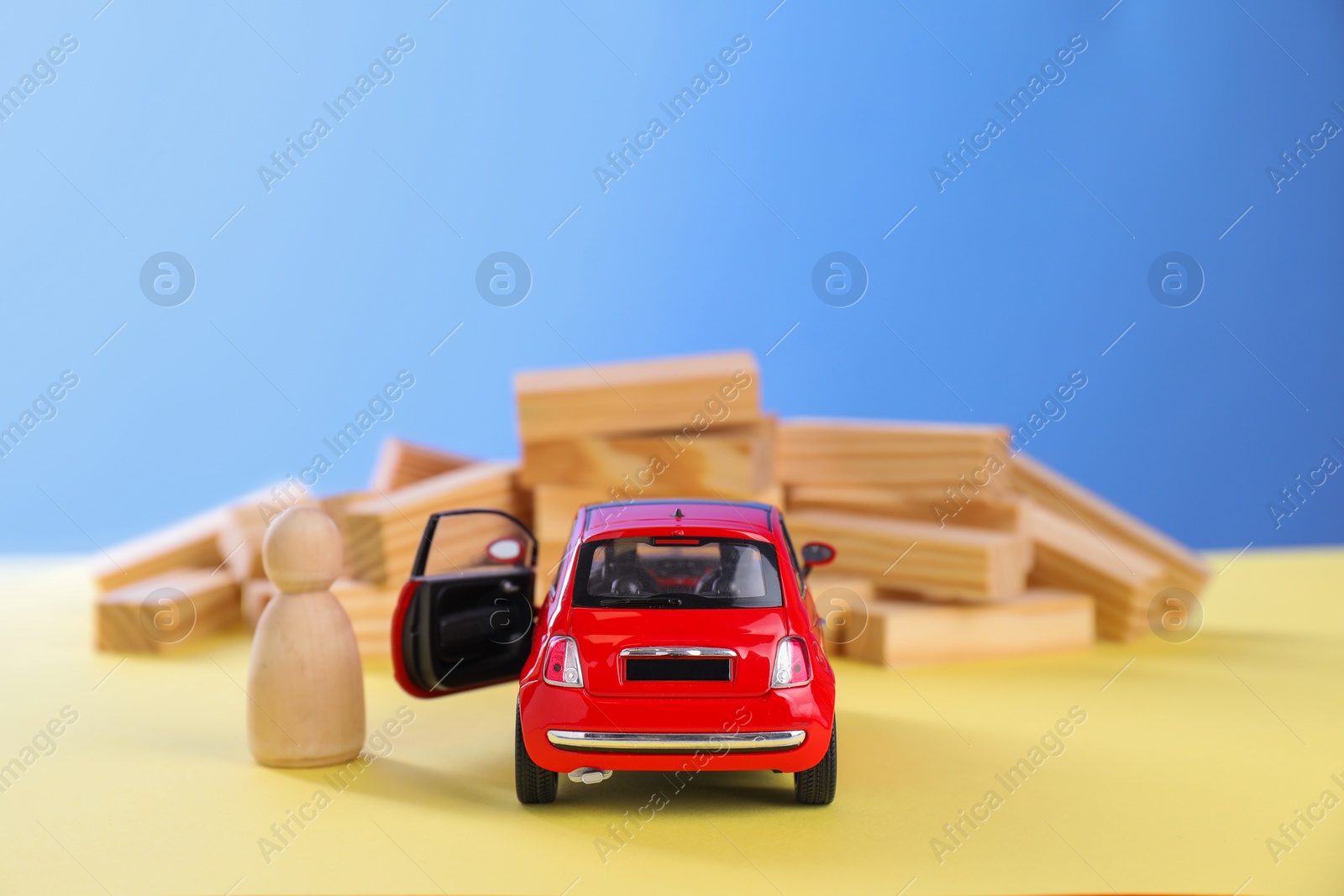 Photo of Overcoming barries for development and success. Wooden human figure near red toy car in front of blocks on yellow surface, space for text.