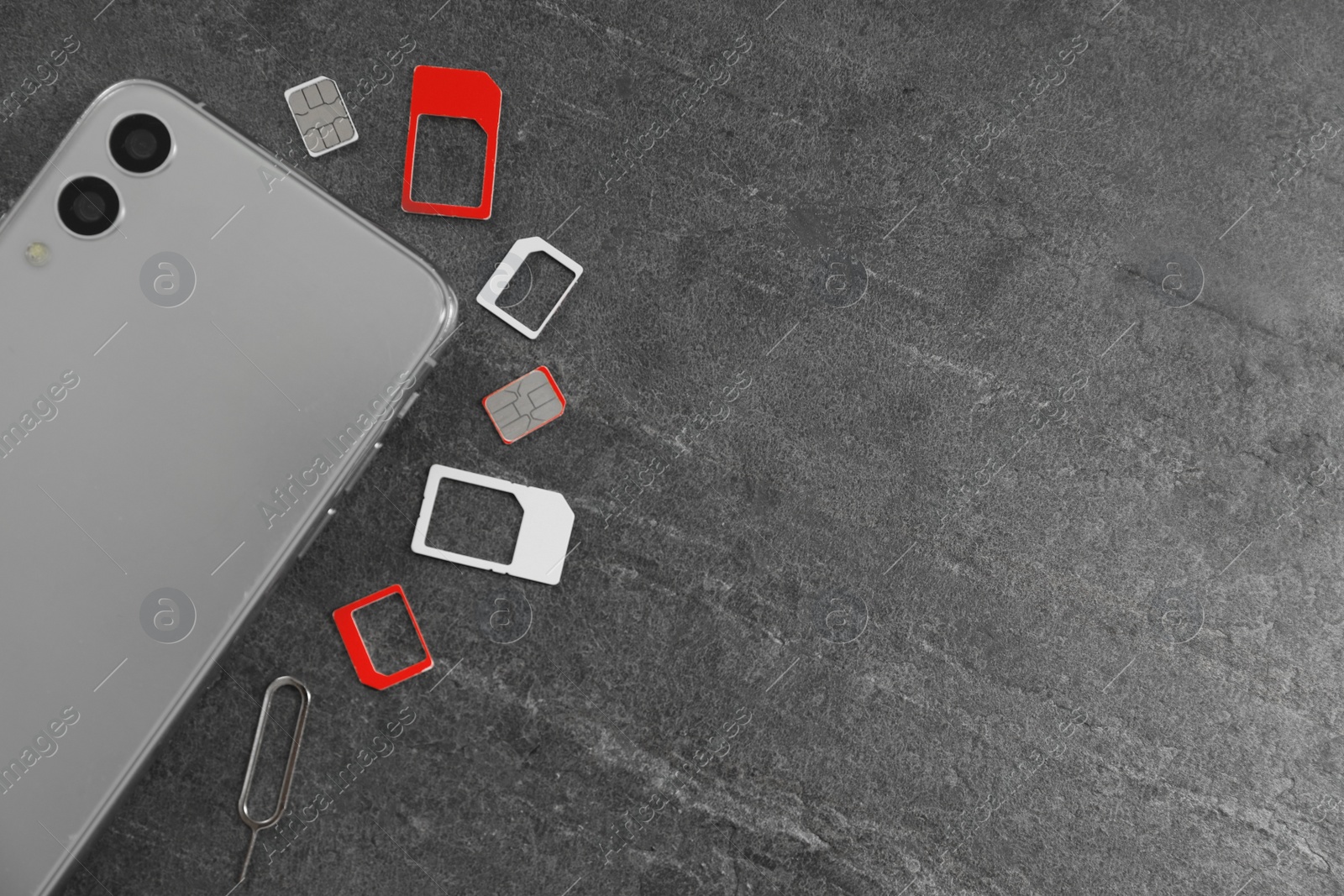 Photo of SIM cards, mobile phone and ejector tool on grey table, flat lay. Space for text