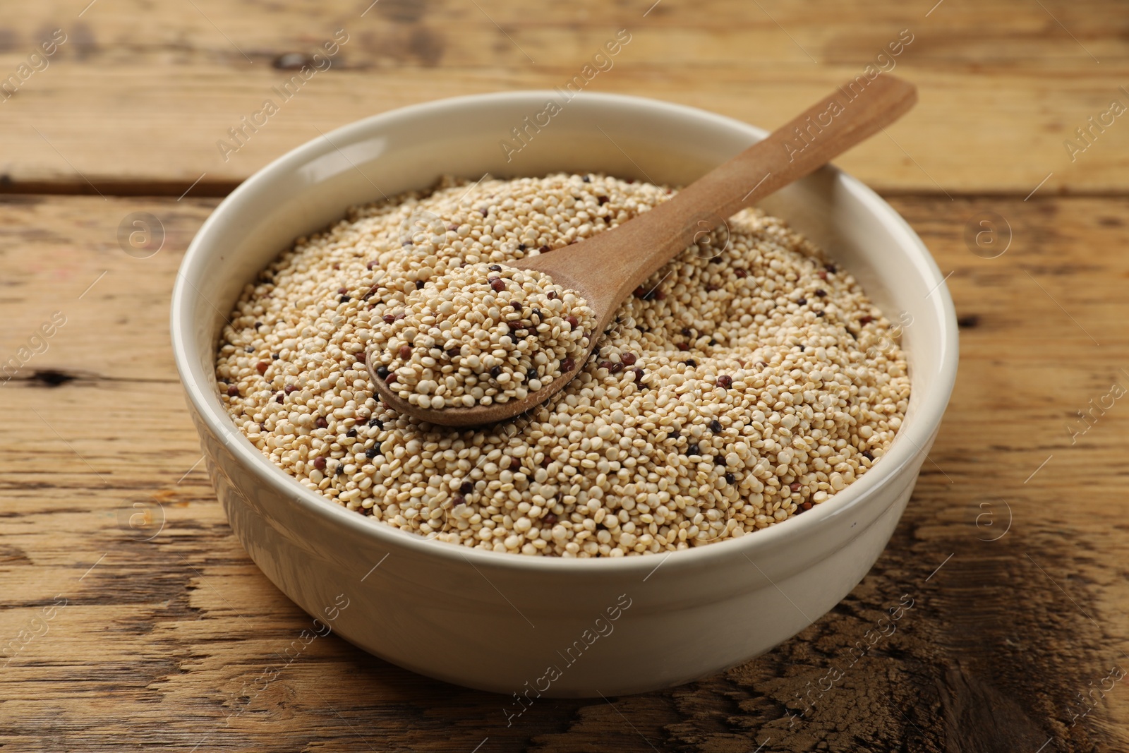 Photo of Raw quinoa seeds and spoon in bowl on wooden table, closeup