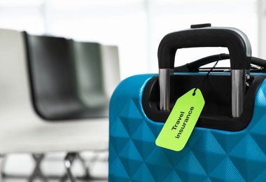 Photo of Blue suitcase with TRAVEL INSURANCE label indoors, closeup. Space for text
