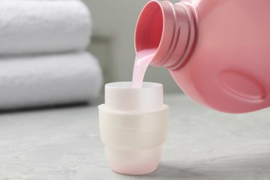 Photo of Pouring laundry detergent from bottle into cap on light grey marble table, closeup