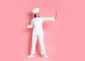 Photo of Happy confectioner with rolling pin and whisk on pink background