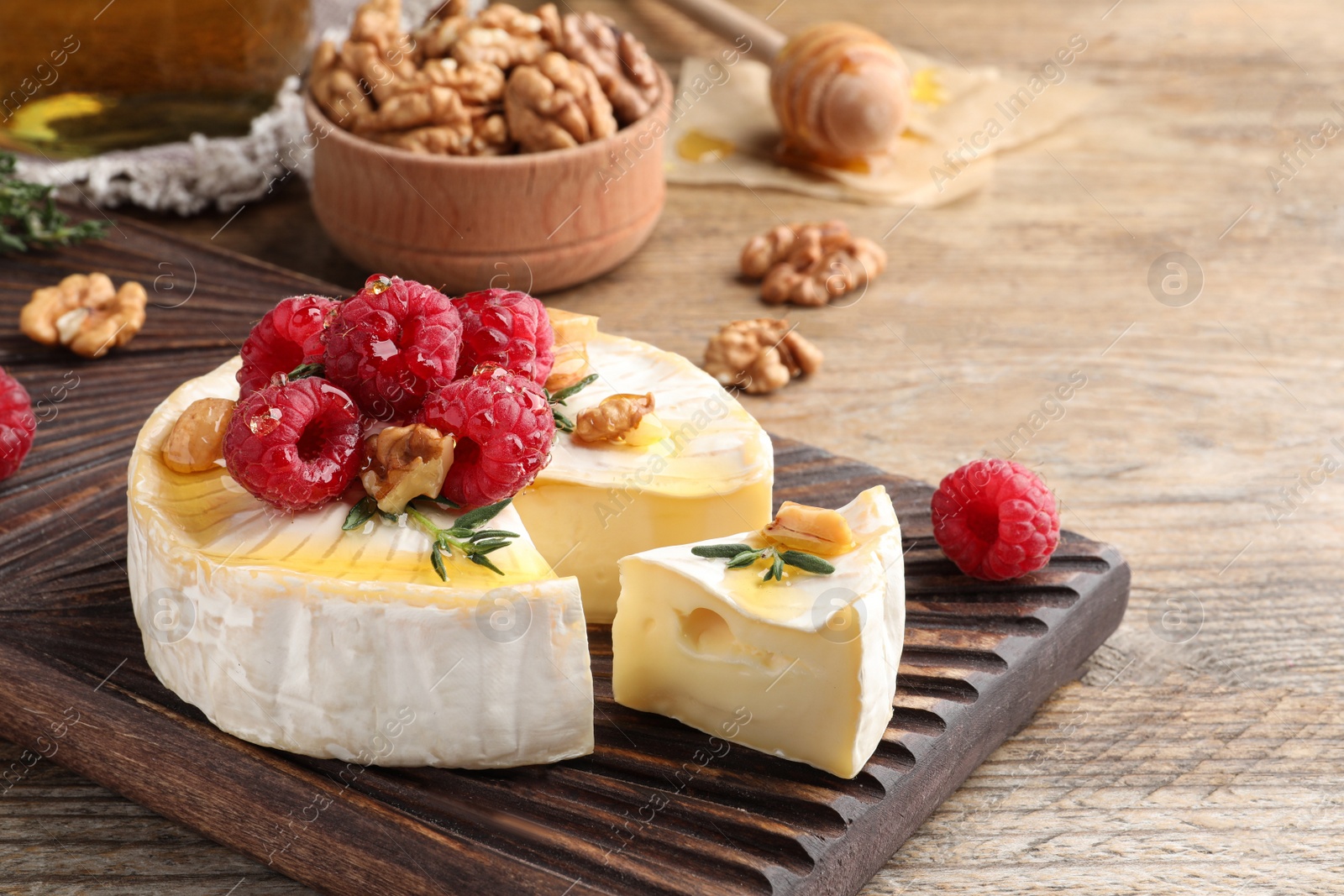 Photo of Brie cheese served with raspberries, walnuts and honey on wooden table. Space for text