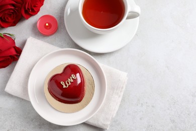 Photo of St. Valentine's Day. Delicious heart shaped cake, tea and roses on light table, flat lay. Space for text