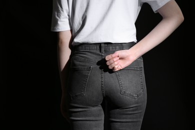 Photo of SOS gesture. Woman showing signal for help behind her back on black background, back view