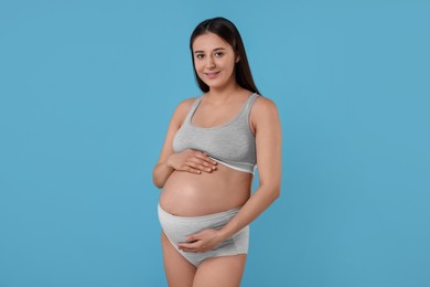 Photo of Beautiful pregnant woman in comfortable maternity underwear on light blue background