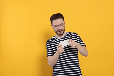 Photo of Emotional man playing game on phone against orange background