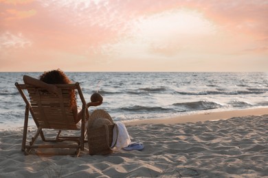 Photo of Woman with cocktail resting in wooden sunbed on tropical beach at sunset