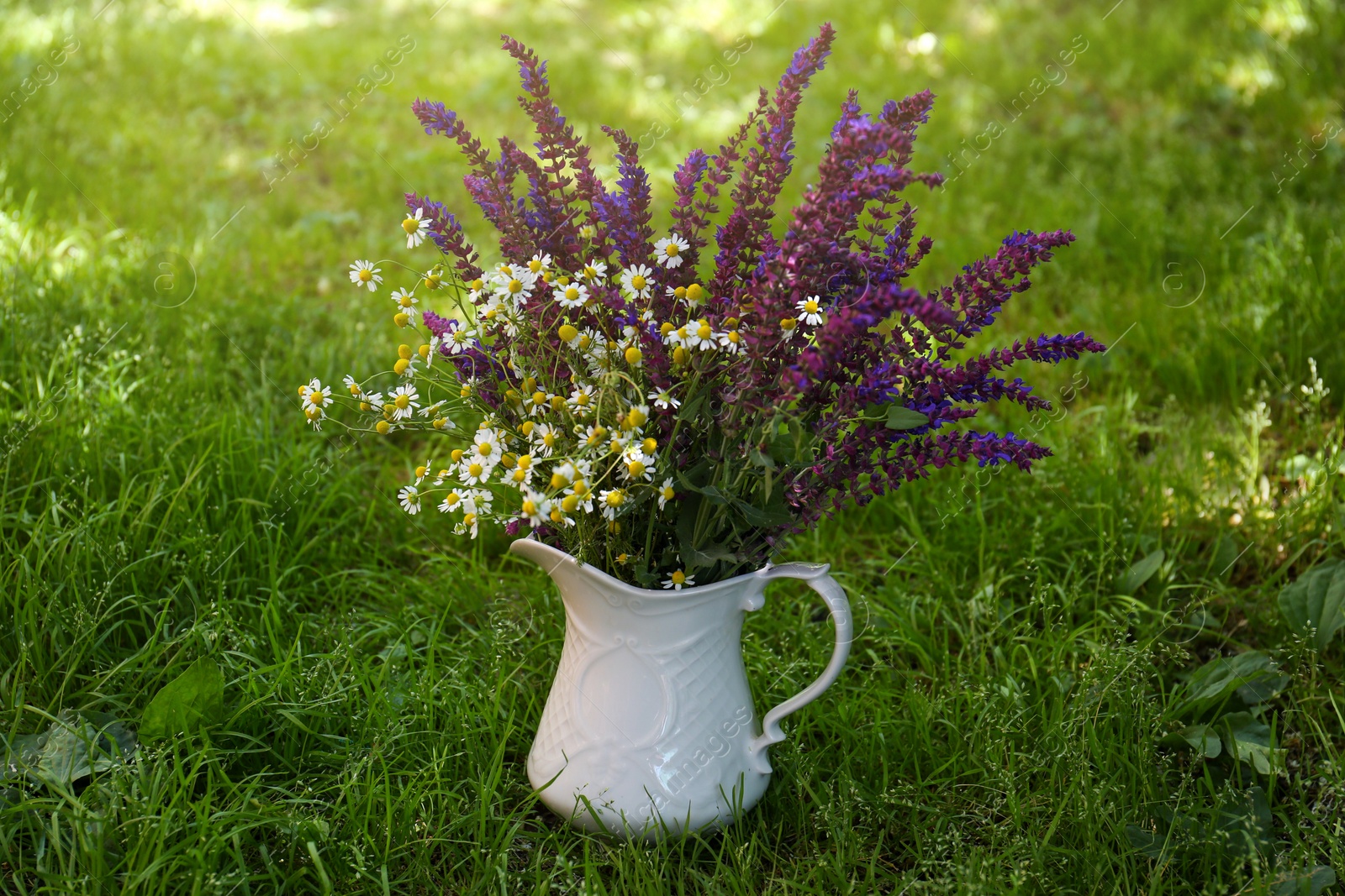 Photo of Beautiful bouquet with field flowers in jug on green grass