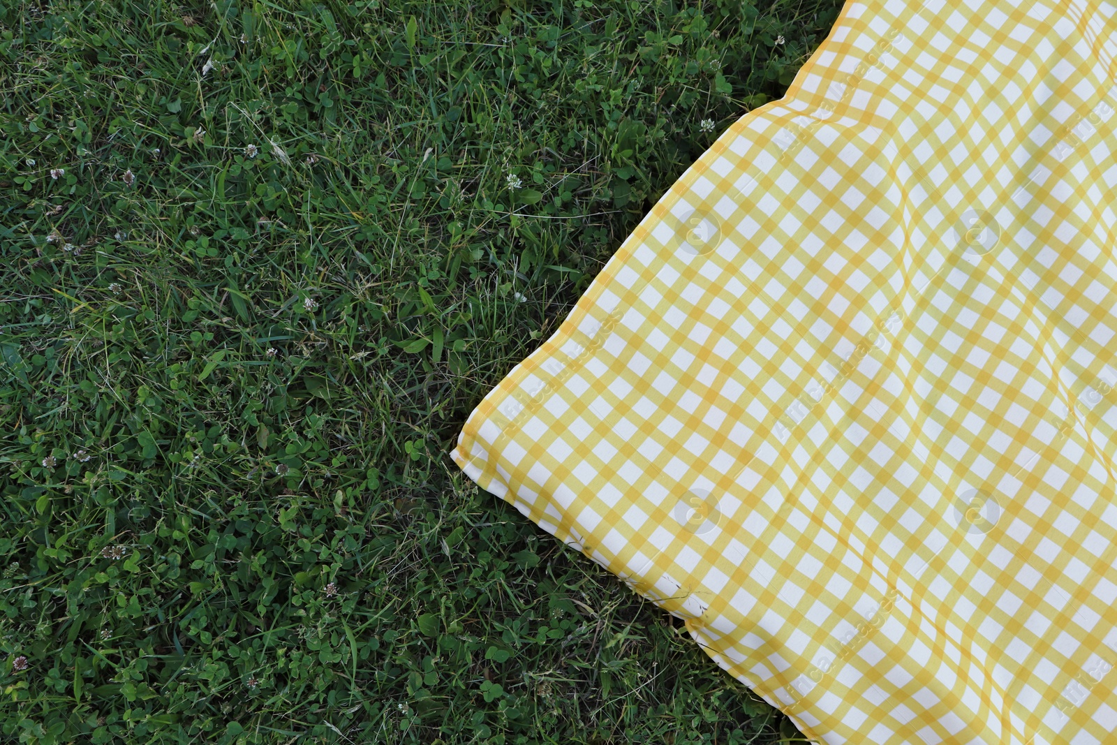 Photo of Checkered picnic tablecloth on fresh green grass, top view. Space for text