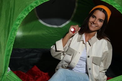 Young woman with flashlight in tent at night