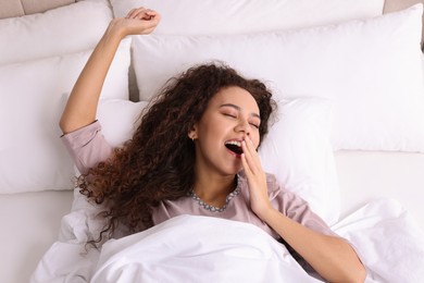 Photo of Happy African American woman awakening in bed, top view