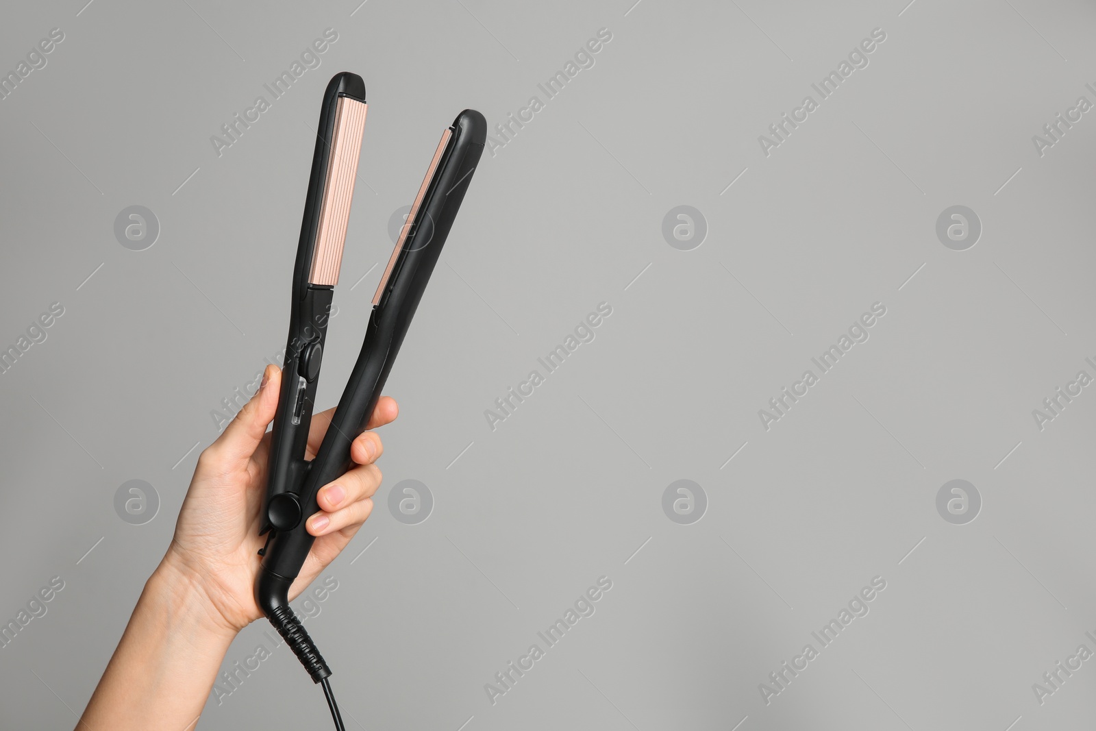 Photo of Woman holding corrugated hair iron on light grey background, closeup. Space for text