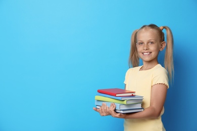 Portrait of cute little girl with books on blue background, space for text. Reading concept