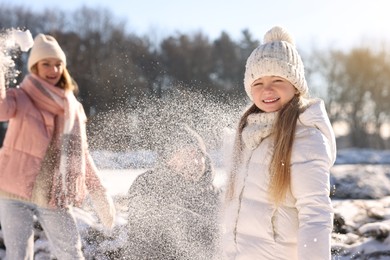 Photo of Portrait of smiling little girl and her family playing with snow in sunny winter park. Space for text