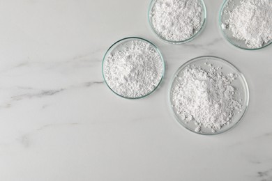 Photo of Many petri dishes with calcium carbonate powder on white marble table, flat lay. Space for text