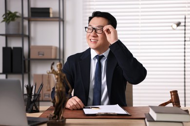 Happy notary writing notes at wooden table in office