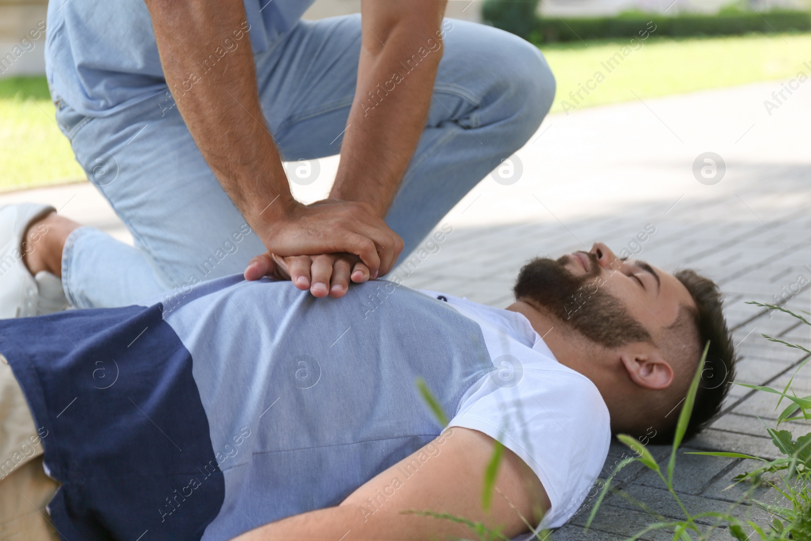 Photo of Passerby performing CPR on unconscious young man in park. First aid