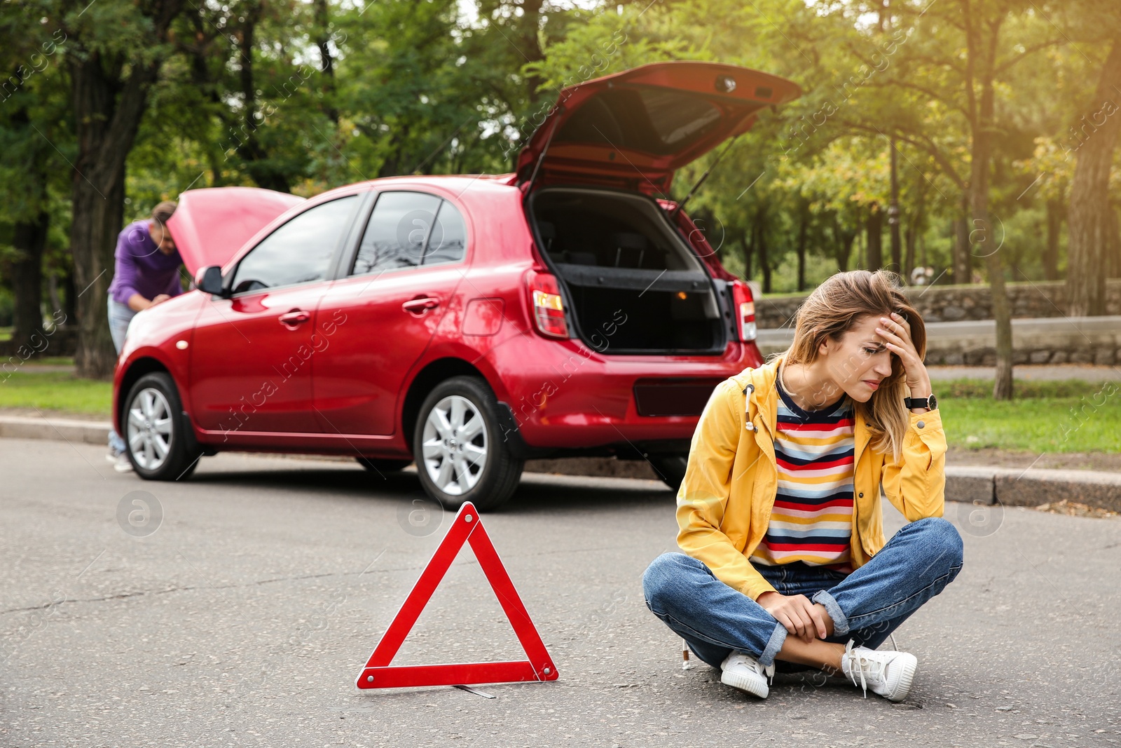 Photo of Upset woman sitting near warning triangle and broken car on road