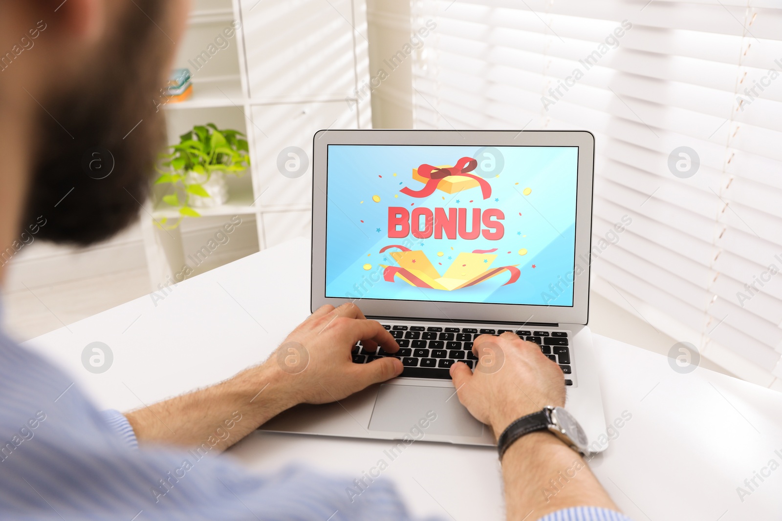 Image of Bonus gaining. Man using laptop at white table indoors, closeup. Illustration of open gift box, word and confetti on device screen