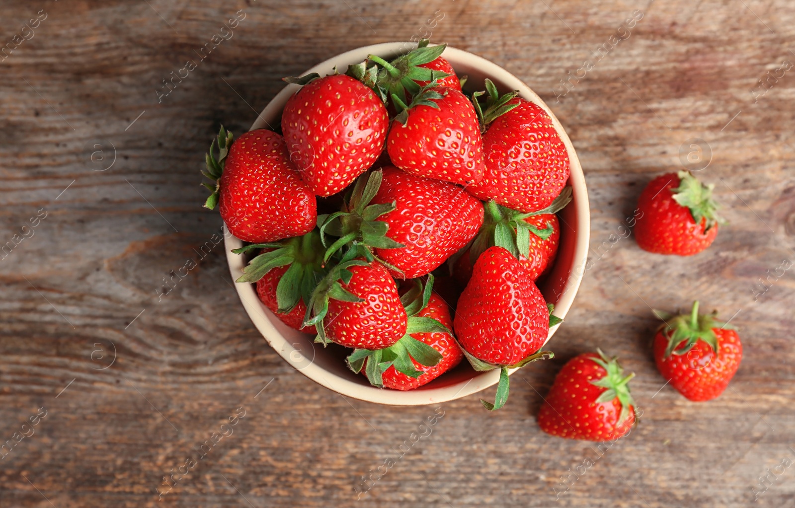 Photo of Bowl with ripe red strawberries on wooden background, top view