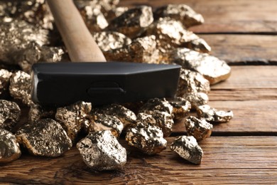 Photo of Pile of gold nuggets and hammer on wooden table, closeup